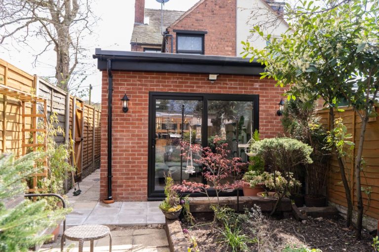 Compact brick rear extension with black-framed sliding doors, opening into a cosy garden space filled with plants and greenery. A stylish upgrade to a traditional home, ideal for extra living or garden room use.