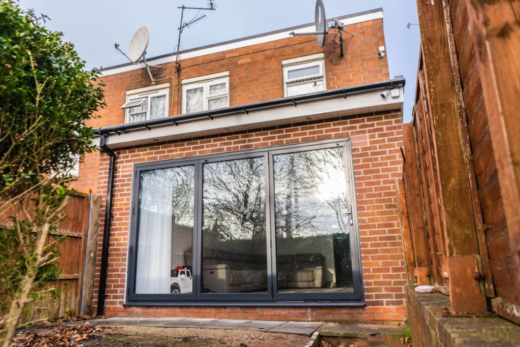 Small rear extension with red brick walls and black-framed sliding glass doors, adding extra living space to a terraced home. The extension opens onto a narrow garden area enclosed by fencing.