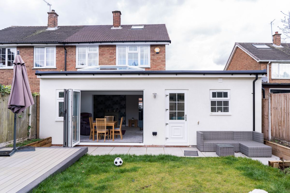 A single-storey rear extension on a semi-detached home, featuring bifold doors, a white exterior finish, and a roof lantern for added natural light. The open-plan space connects to the garden, creating a bright, modern dining area.