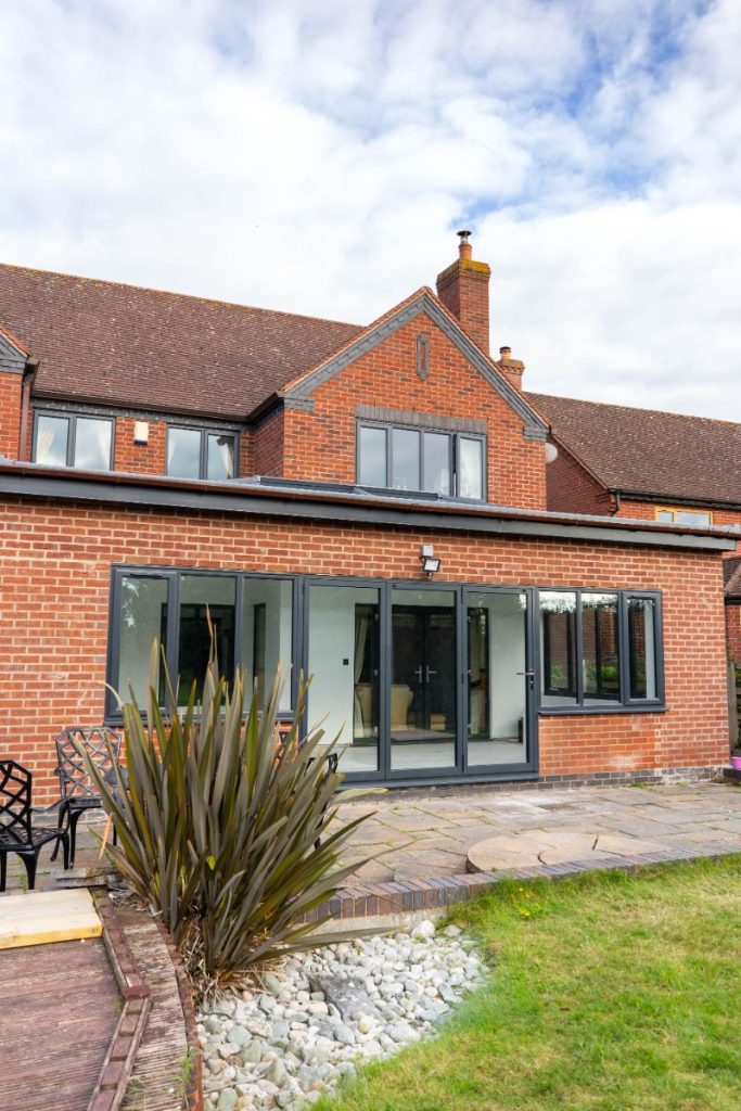 Brick-built single-storey extension with dark grey bifold doors and matching windows, seamlessly blending with the style of this traditional home. The extension opens onto a paved patio and landscaped garden.