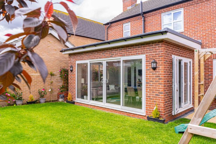 Attractive brick home extension in West Midlands with large sliding patio doors and bi-fold doors, opening to a green garden. Perfect for local home improvements.
