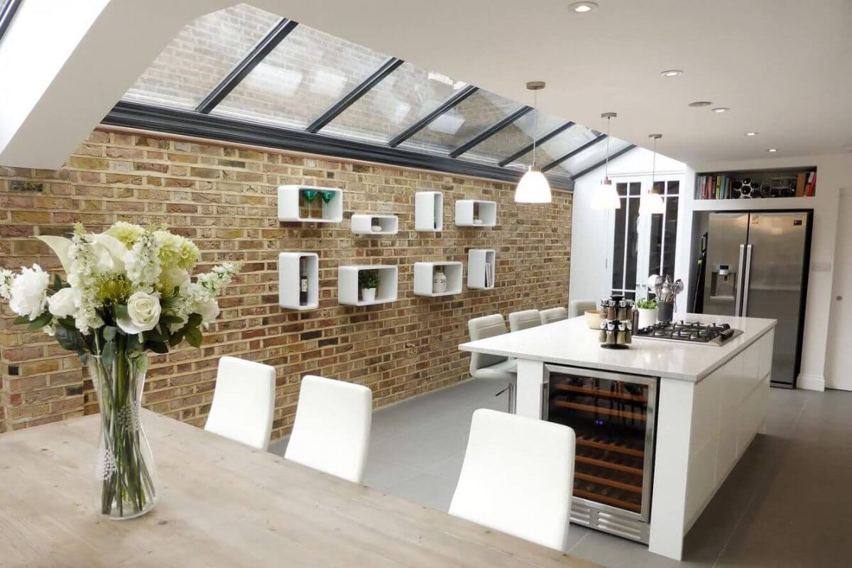 Modern side return extension with exposed brick wall, roof glazing, and a bright open-plan kitchen and dining space in a London home.