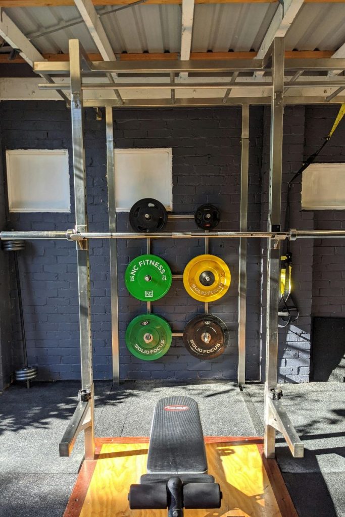 A garage lifting rack with colours weights and a lifting bench