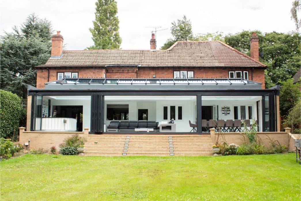 brick house featuring a contemporary glass extension with bi-fold doors, leading to a lush green lawn and garden