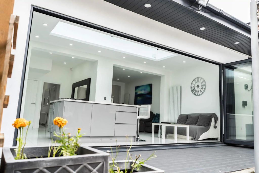 bright, contemporary open-plan kitchen extension and living area featuring stylish grey cabinetry, a comfortable sofa, and seamless access to the outdoors via sleek bi-fold doors