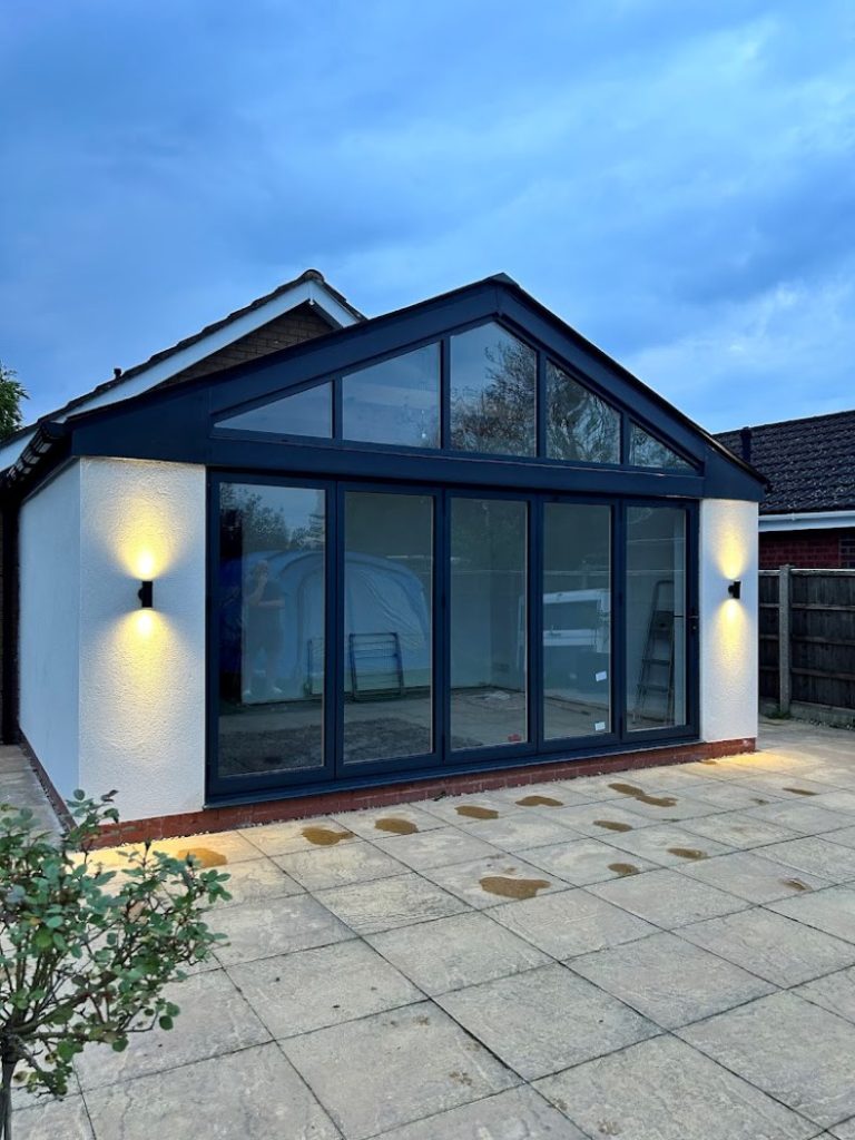 single storey extension with black bifold doors lit up by lights either side