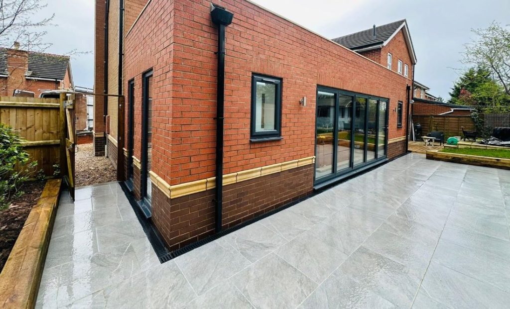 Contemporary red brick house extension featuring large bi-fold doors, a newly installed light grey tiled patio, and integrated drainage system