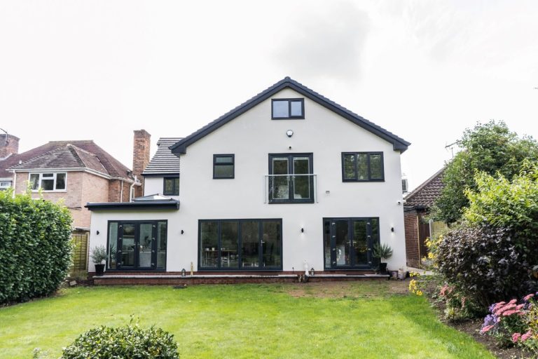 Stunning rear view of a contemporary white house featuring rear extension with large bi-fold doors, a balcony, and a well-maintained green lawn and garden