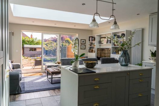 Bright and airy open-plan kitchen and living room extension featuring a large skylight, kitchen island, and sliding doors to a green garden.